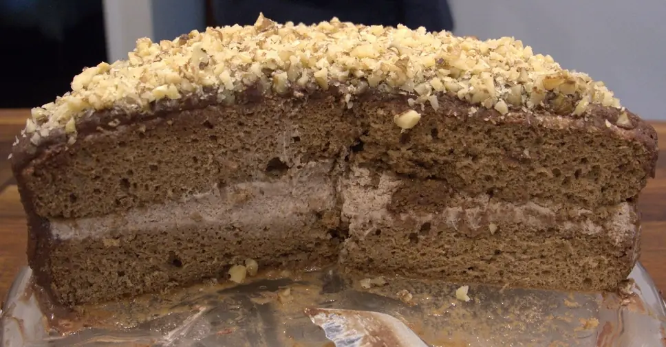 Cross-section of the cake, showing two sponge cake layers, a thick middle layer of whipped cream, ganache coating and chopped walnut topping.