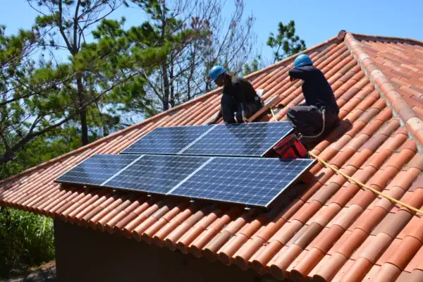 Two people installing solar panels on a roof.