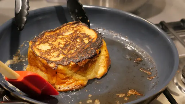 A crispy, thick piece of french toast frying in a pan.